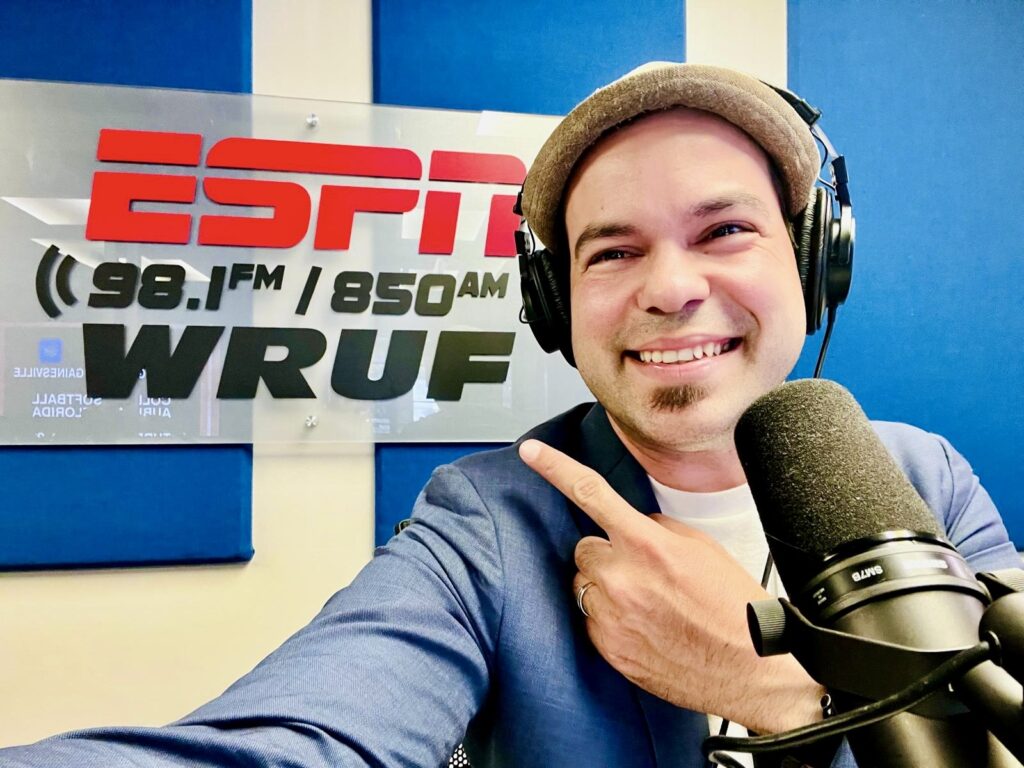 Elio Piedra at the ESPN WRUF studio smiling to the camera